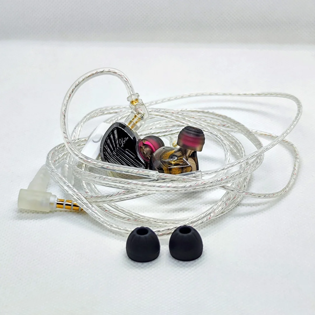 The GK KUNTEN IEMs connected to their stock silver braided audio cable, arranged neatly on a white background. The earpieces are fitted with aftermarket silicone eartips featuring a translucent grey flange and a pink core. In the foreground, a pair of black stock KZ Starline eartips sits separately. The right-angled 3.5mm jack is visible on the left.